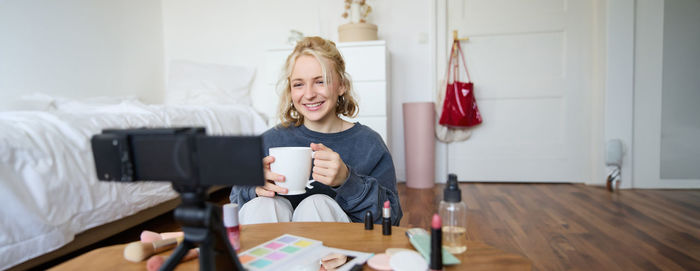 Young woman using mobile phone while sitting on bed at home