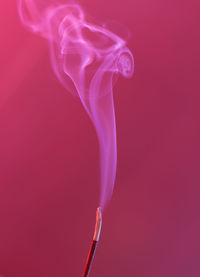 Close up of incense emitting smoke against pink wall