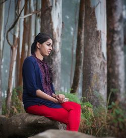 Side view of young woman sitting on tree trunk in forest
