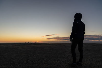 Rear view of silhouette woman at beach against sky during sunset