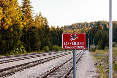 Road sign by railroad tracks against clear sky