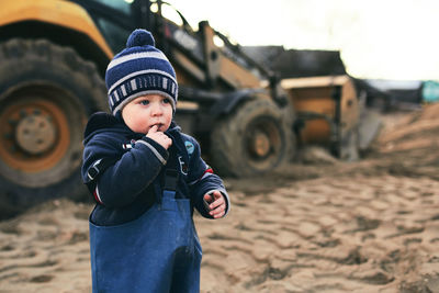 A boy in the village on the background of a tractor walks on the sand . 