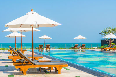 Lounge chairs with parasol by swimming pool against clear sky