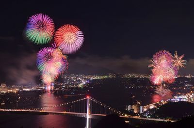 Bridge over sea against firework display at night