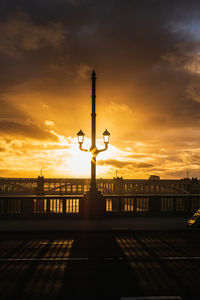 Silhouette street lights against orange sky during sunset