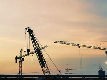 Low angle view of cranes at construction site against sky during sunset