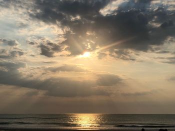 Sunlight streaming through clouds over sea during sunset