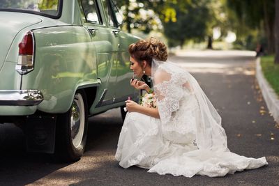 Side view of bride applying lipstick by car