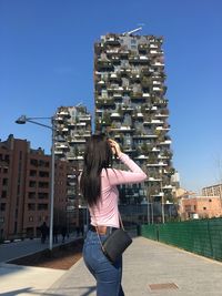 Woman looking towards buildings while standing on footpath in city