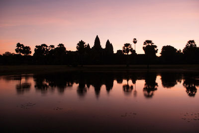 Silhouette trees by lake against sky during sunset