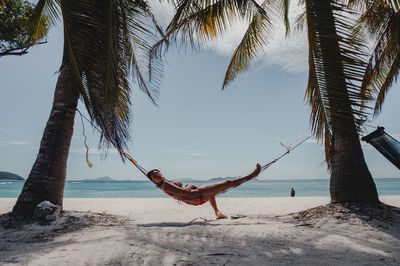 Woman lying on hammock at beach against sky