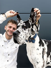 Playful male owner having fun with harlequin great dane dog during stroll in city and looking at camera