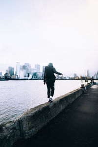 Rear view of man walking on retaining wall by river