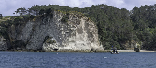 Scenic view of tall cliffs facing the sea against sky with scuba divers and boat