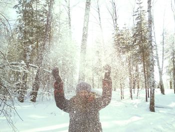 Woman throwing snow up in the air in winter forest