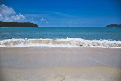 Waves of the azure andaman sea under the blue sky reaching the shores of cenang beach in langkawi