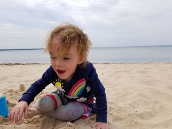 Cute girl playing with sand at beach against sky