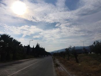 Empty road along trees and plants against sky