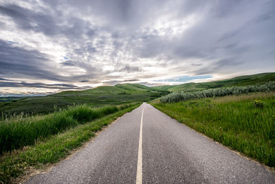 Empty road amidst field against sky