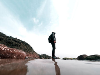 Man standing on rock looking at sea against sky