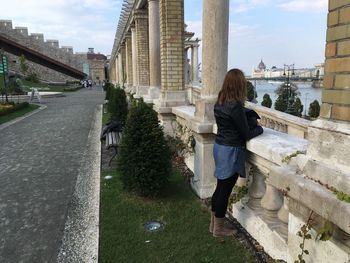 Rear view of woman standing by retaining wall against sky in city