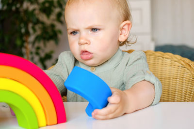 Little baby child in clothes made of natural fabric plays with rainbow colored wooden toys at table