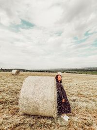 Woman standing by hay bales on field against sky