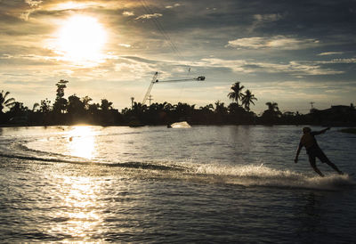 Silhouette man in sea against sky during sunset