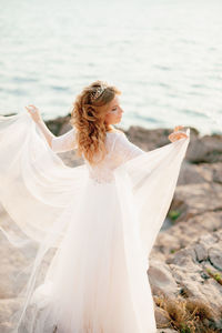 Rear view of woman standing on rock near sea