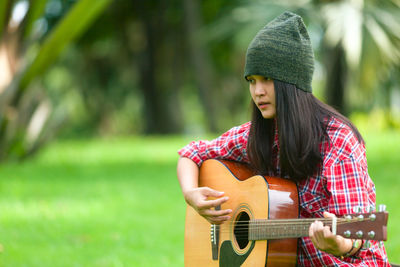 Thoughtful young woman playing acoustic guitar at park