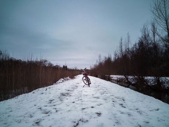 Man riding bicycle on snow covered field against sky