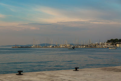 Sailboats moored in harbor at sunset