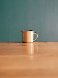 A cup made of tin, with a spoon on top, which is placed on a wooden table. 
