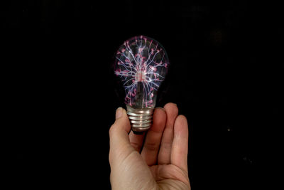 Close-up of hand holding illuminated light bulb against black background
