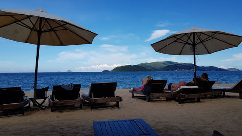 Lounge chairs and tables on beach against sky