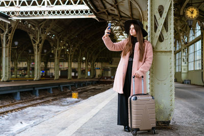 Happy young woman on platform of railway station in pink coat and black hat