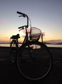 Bicycle by sea against sky during sunset