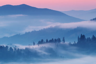 Scenic view of fog covered mountains against sky during sunrise