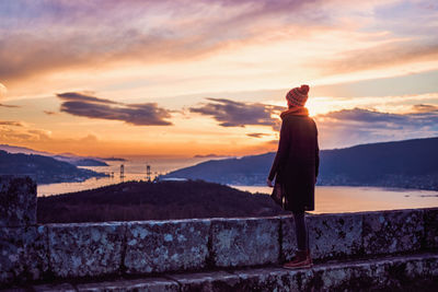 Rear view of woman standing on mountain against sky during sunset