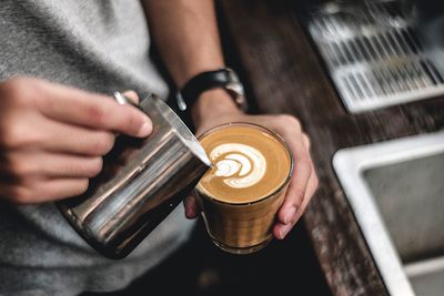 Midsection of man pouring milk in coffee cup