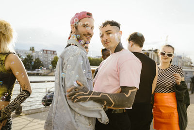 Side view portrait of gay man standing with non-binary person on promenade in city