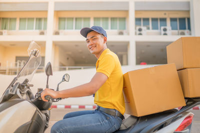 Portrait of smiling delivery man sitting with parcels on scooter