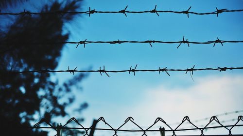 Close-up of barbed wires fence against sky