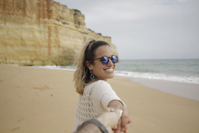 Young woman smiling while standing on beach against sky