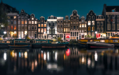 Boats moored in river against buildings in city at night