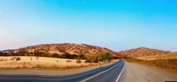 Road leading towards mountains against clear blue sky