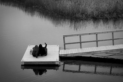 Rear view of people sitting on pier over lake