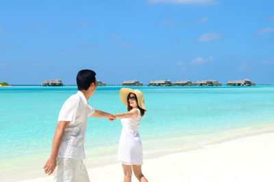 Couple with holding hands walking at beach against sky