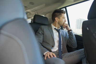 Young businessman looking out the window sitting in car service limousine