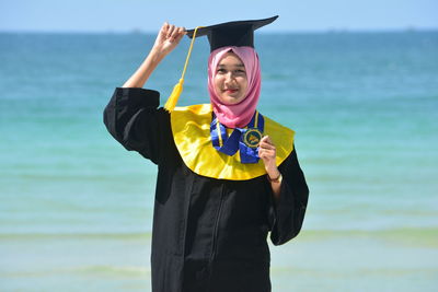 Portrait of woman in hijab wearing mortarboard while standing against sea